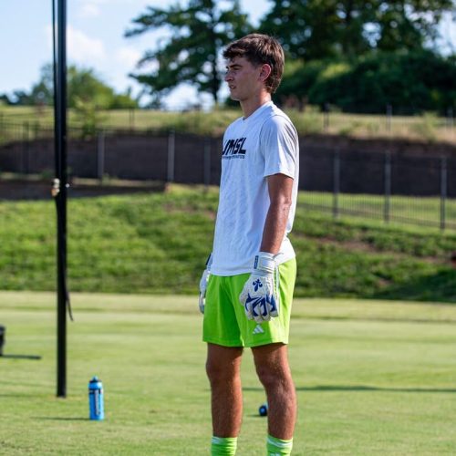 Goalkeeper watching from the sideline in the Fleur De Lis GK Nova Pro OG University Blue Trim.